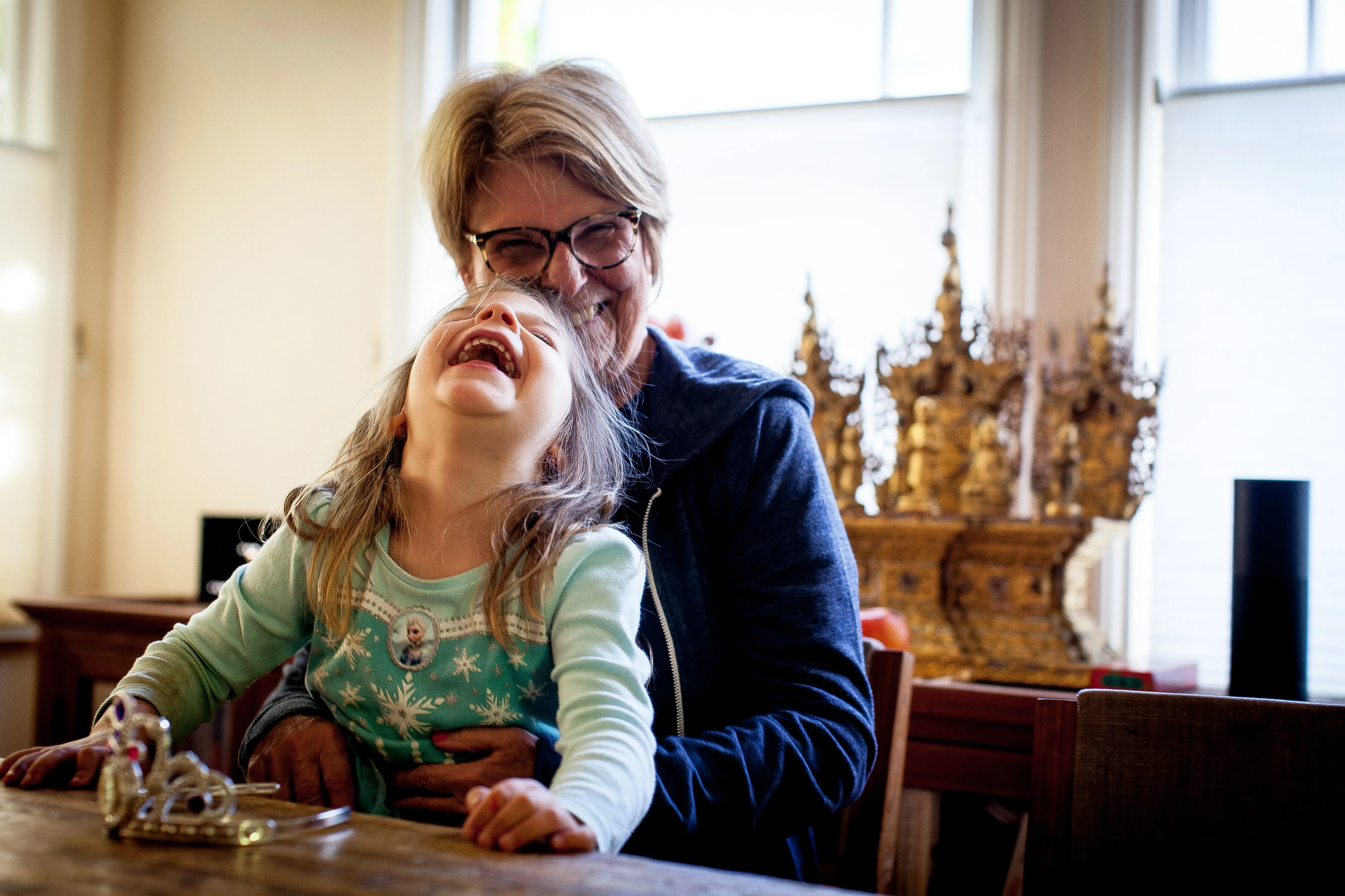 Susan laughing with a delighted young girl on her lap at a table